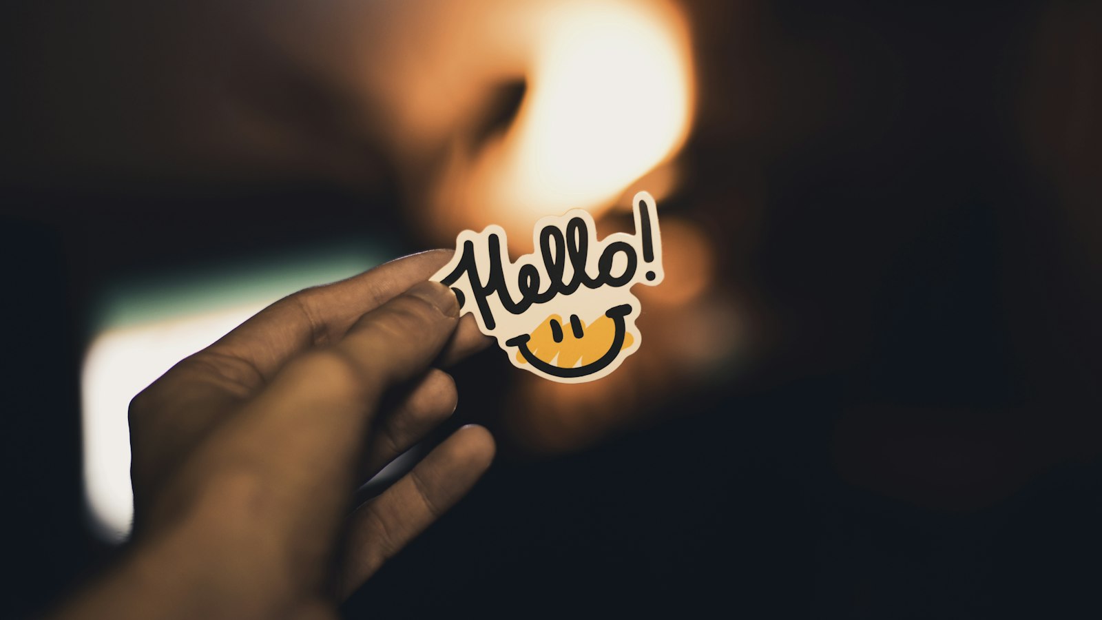 A hand holding a "Hello!" sticker in warm light